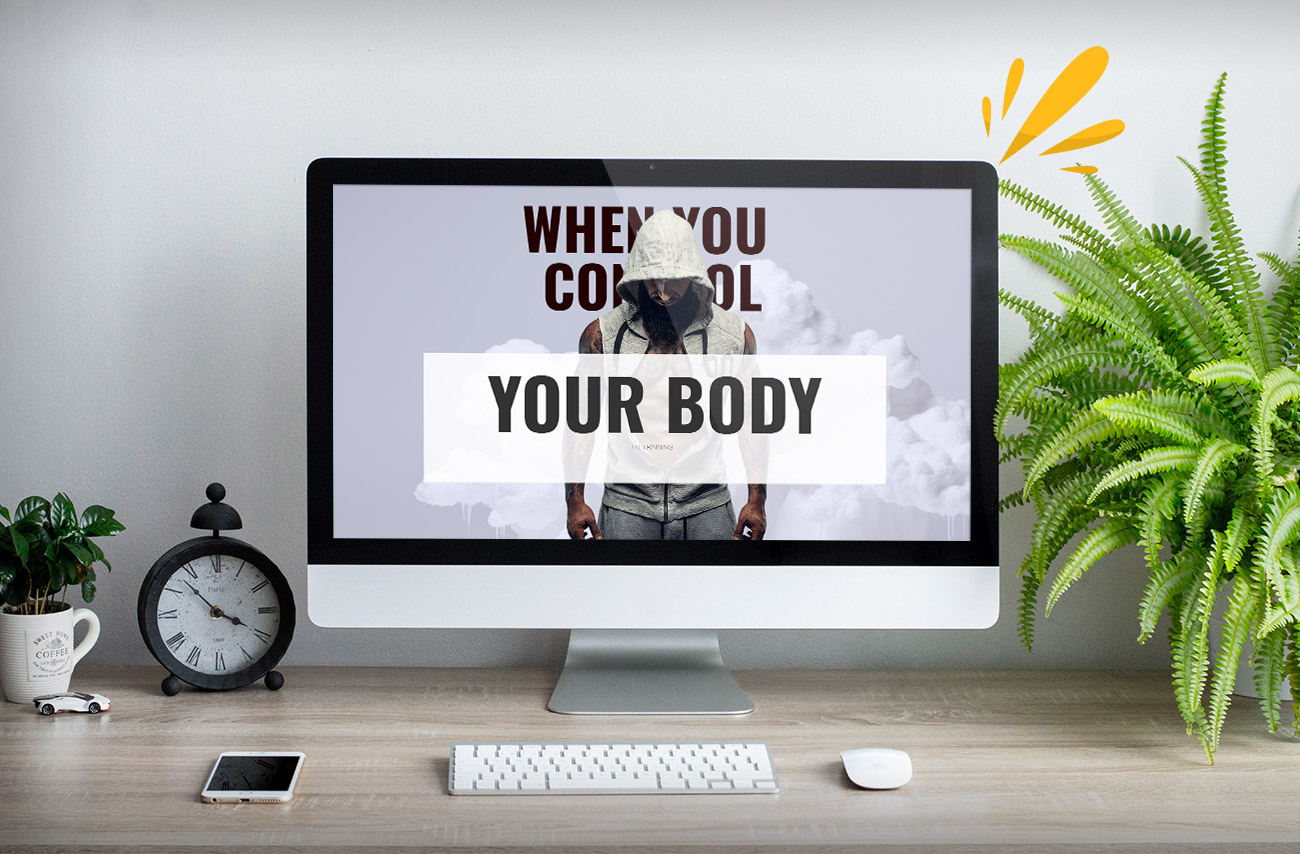 A modern computer monitor displays motivational text about body control, surrounded by a plant, clock, and smartphone on a wooden desk.