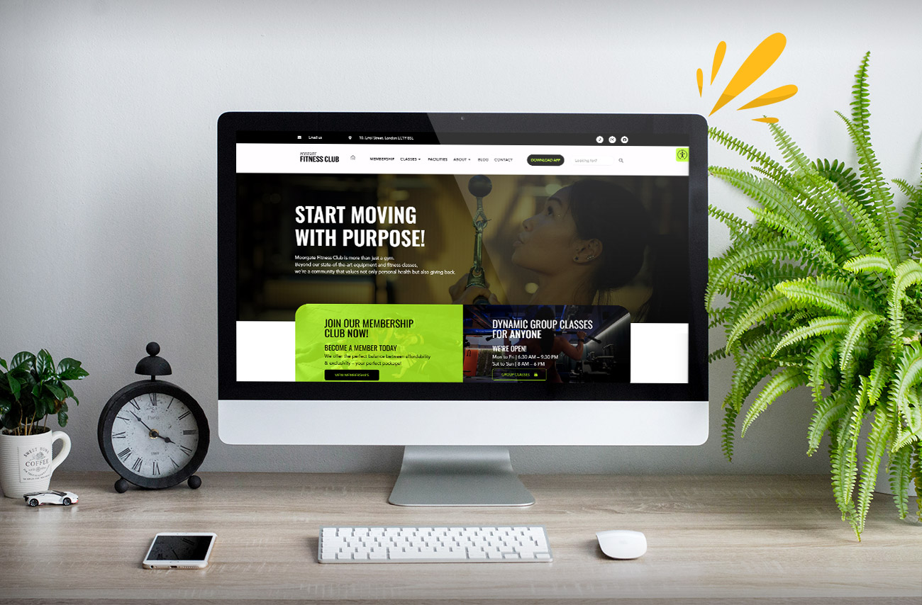 A computer monitor displays a fitness club website, featuring membership info, class schedules, and a decorative plant on a wooden desk.