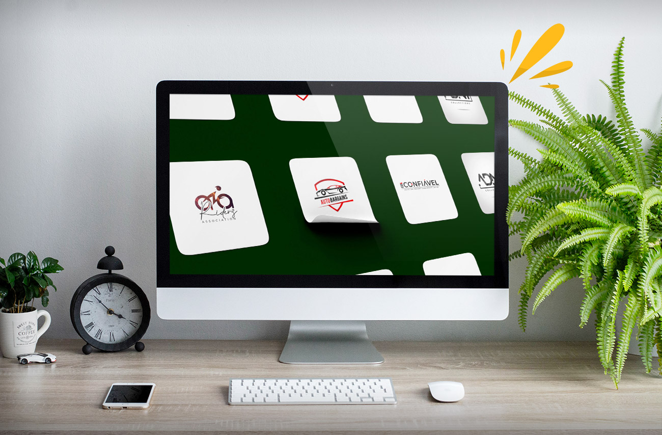 A desktop monitor displays a grid of various logo designs on a dark green background, beside a clock and a plant.